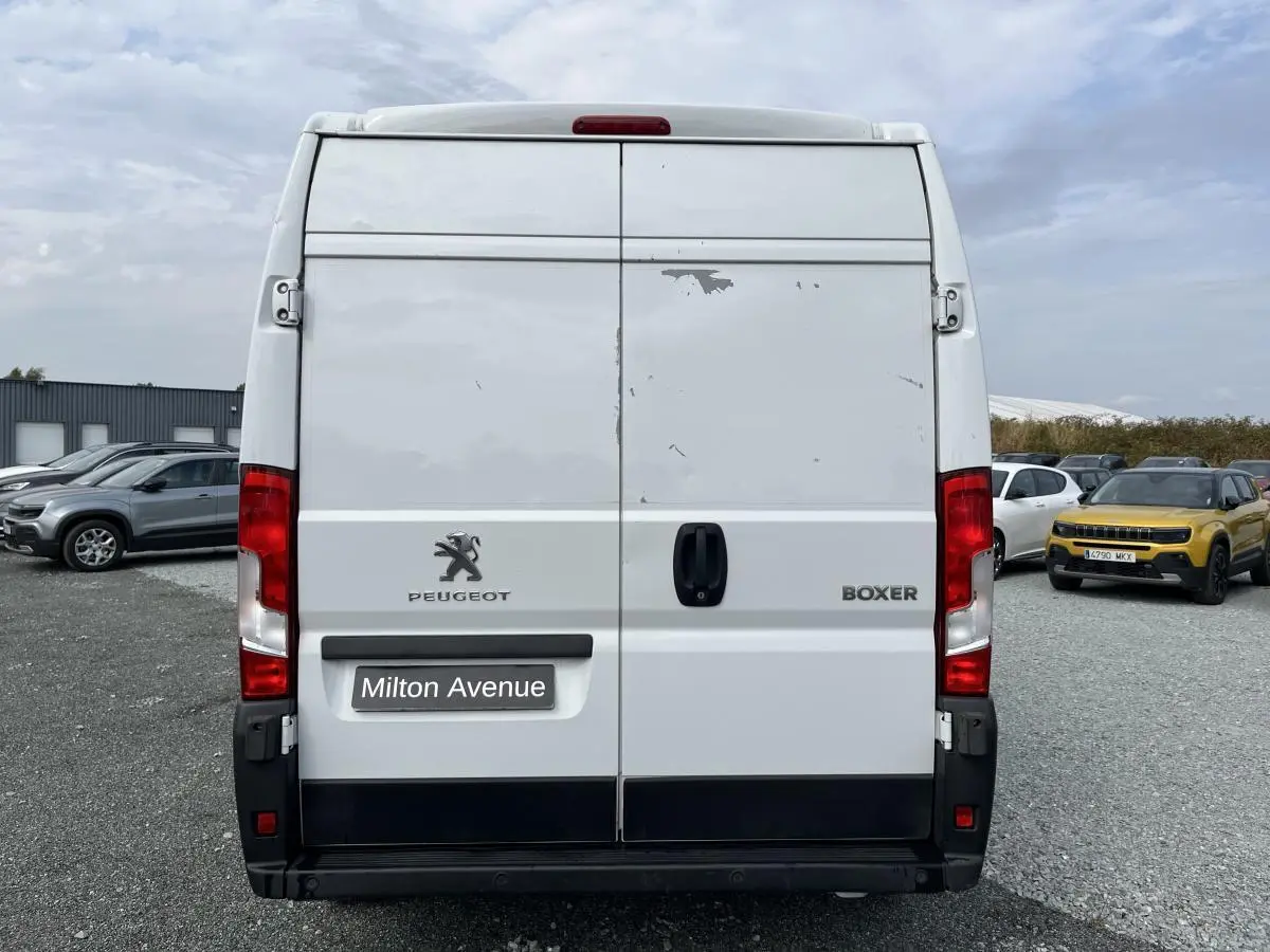 Vue arrière d'un Peugeot Boxer Fourgon blanc avec portes tôlées et logo Peugeot visible, stationné sur un parking.