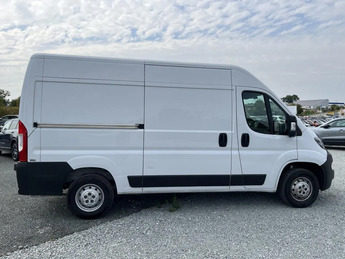 Vue latérale droite d’un Peugeot Boxer Fourgon blanc 2023 avec porte coulissante tôlée et protections noires.