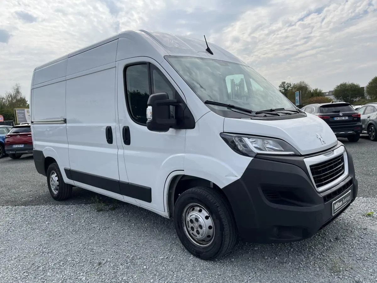 Peugeot Boxer Fourgon blanc en 3/4 avant droit, avec porte latérale coulissante et pare-chocs noirs robustes.