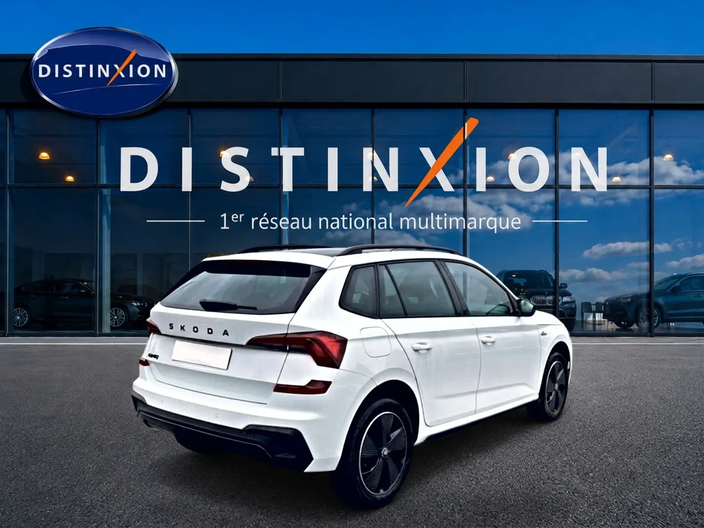 Vue 3/4 arrière droite d'un Skoda Kamiq blanc nacré avec jantes alu noires, devant une vitrine Distinxion.