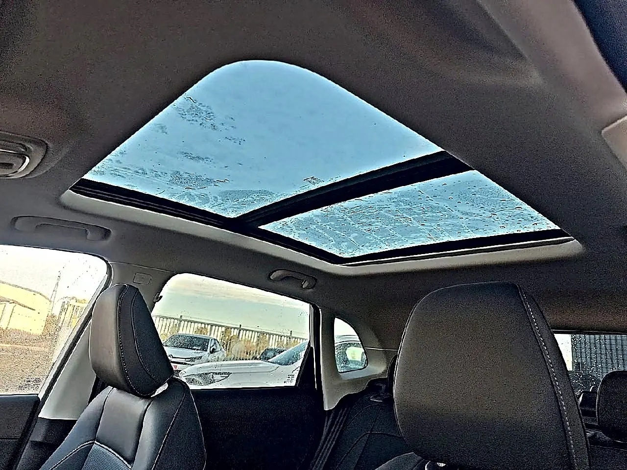 Toit panoramique en verre vu de l'intérieur arrière d'un MG Motor ZS blanc avec sièges en similicuir noir.