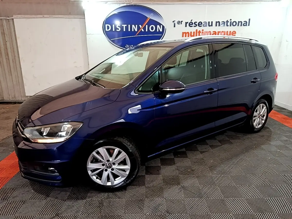 Volkswagen Touran bleu 3/4 avant droit, avec jantes alliage et rétroviseurs noirs brillants en intérieur showroom