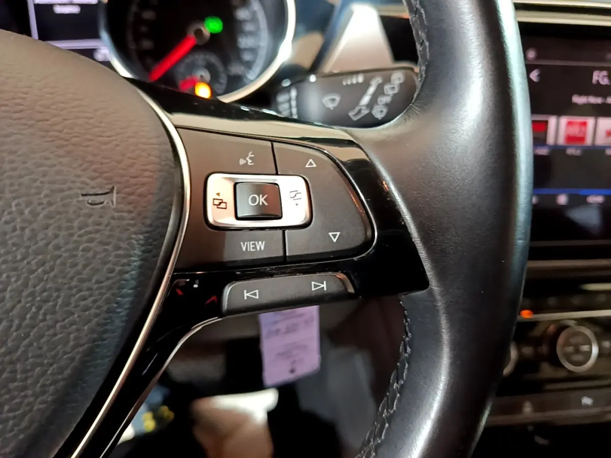 Gros plan sur les commandes au volant cuir côté gauche du Volkswagen Touran bleu, avec tableau de bord et écran tactile en arrière-plan.