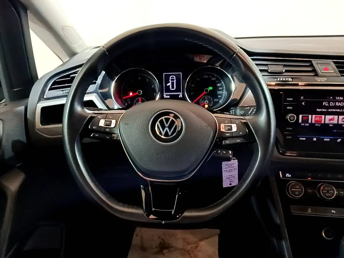 Volant cuir noir vu de face dans l'habitacle d'un Volkswagen Touran bleu, avec écran tactile et commandes au volant.