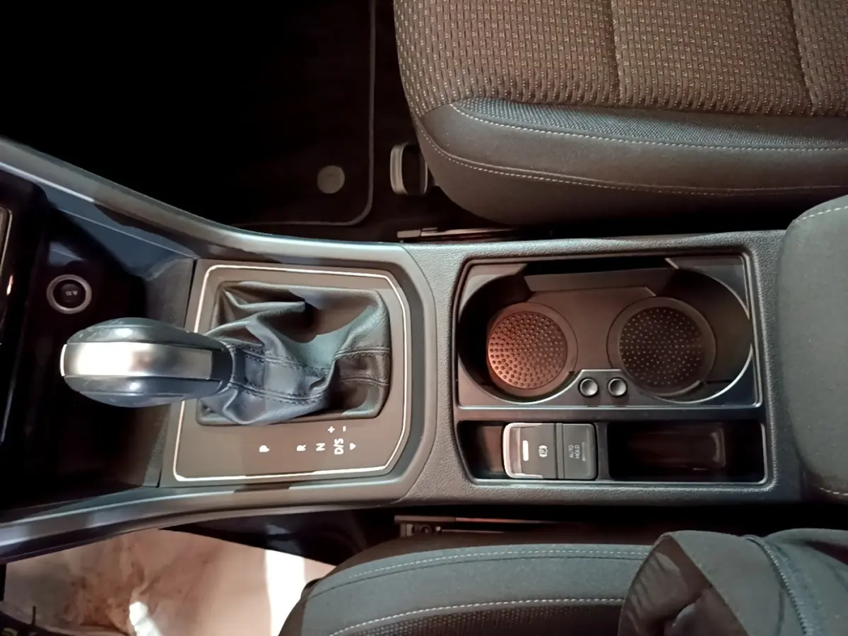 Vue plongeante sur la console centrale noire du Volkswagen Touran 1.5 TSI EVO DSG7 United avec levier de vitesse automatique et porte-gobelets.