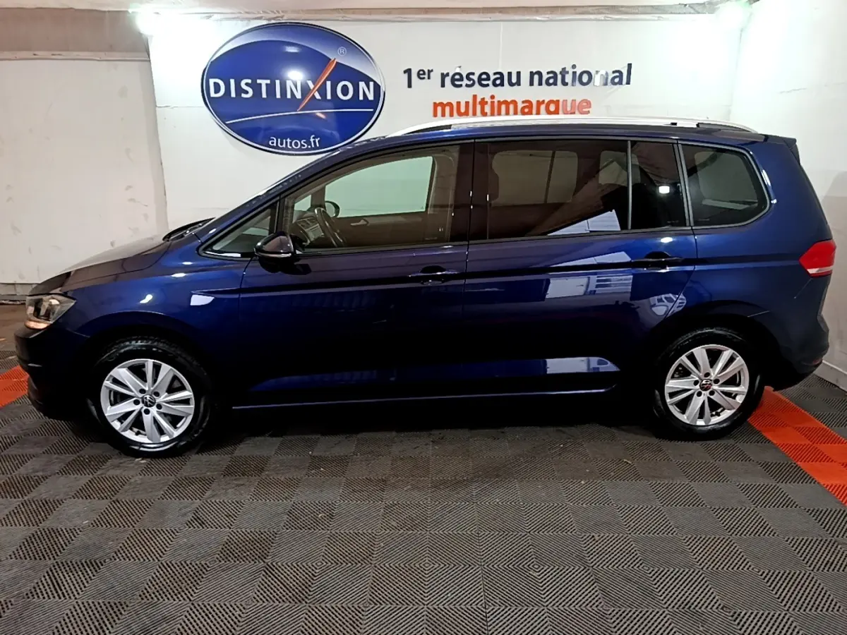 Profil latéral gauche d'un Volkswagen Touran bleu 2021 garé en intérieur avec jantes alliage et vitres teintées.