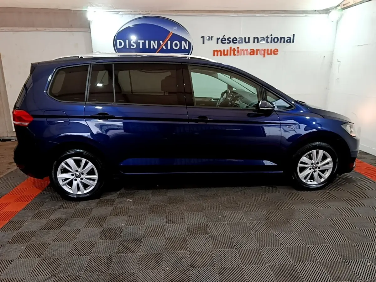 Profil droit d'un Volkswagen Touran bleu 2021 garé en intérieur avec vitres teintées et jantes alliage.