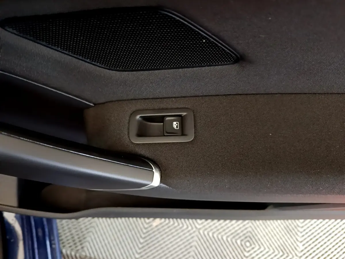 Gros plan sur la poignée intérieure et le bouton de verrouillage de la porte côté gauche d’un Volkswagen Touran bleu.