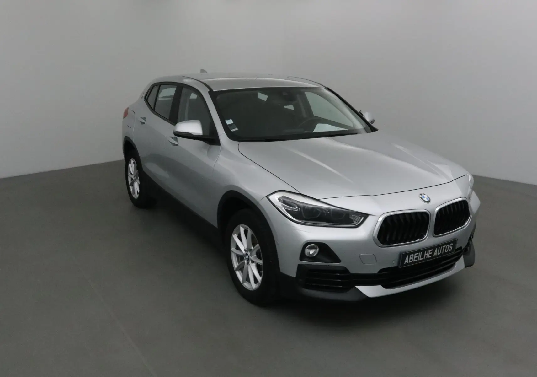 BMW X2 gris clair métal vue 3/4 avant droit dans un studio avec calandre et jantes visibles.