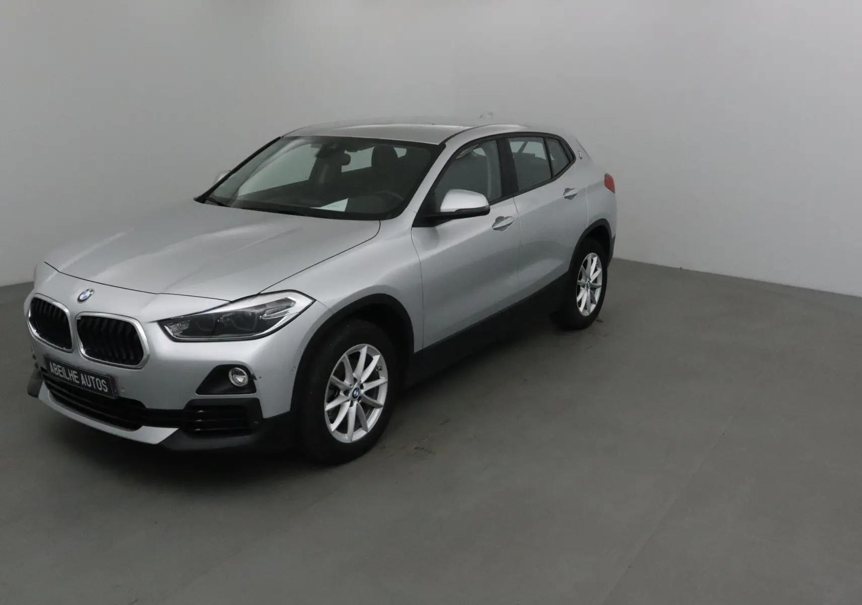BMW X2 gris clair métal vue 3/4 avant droit dans un studio, avec jantes alliage et calandre caractéristique.