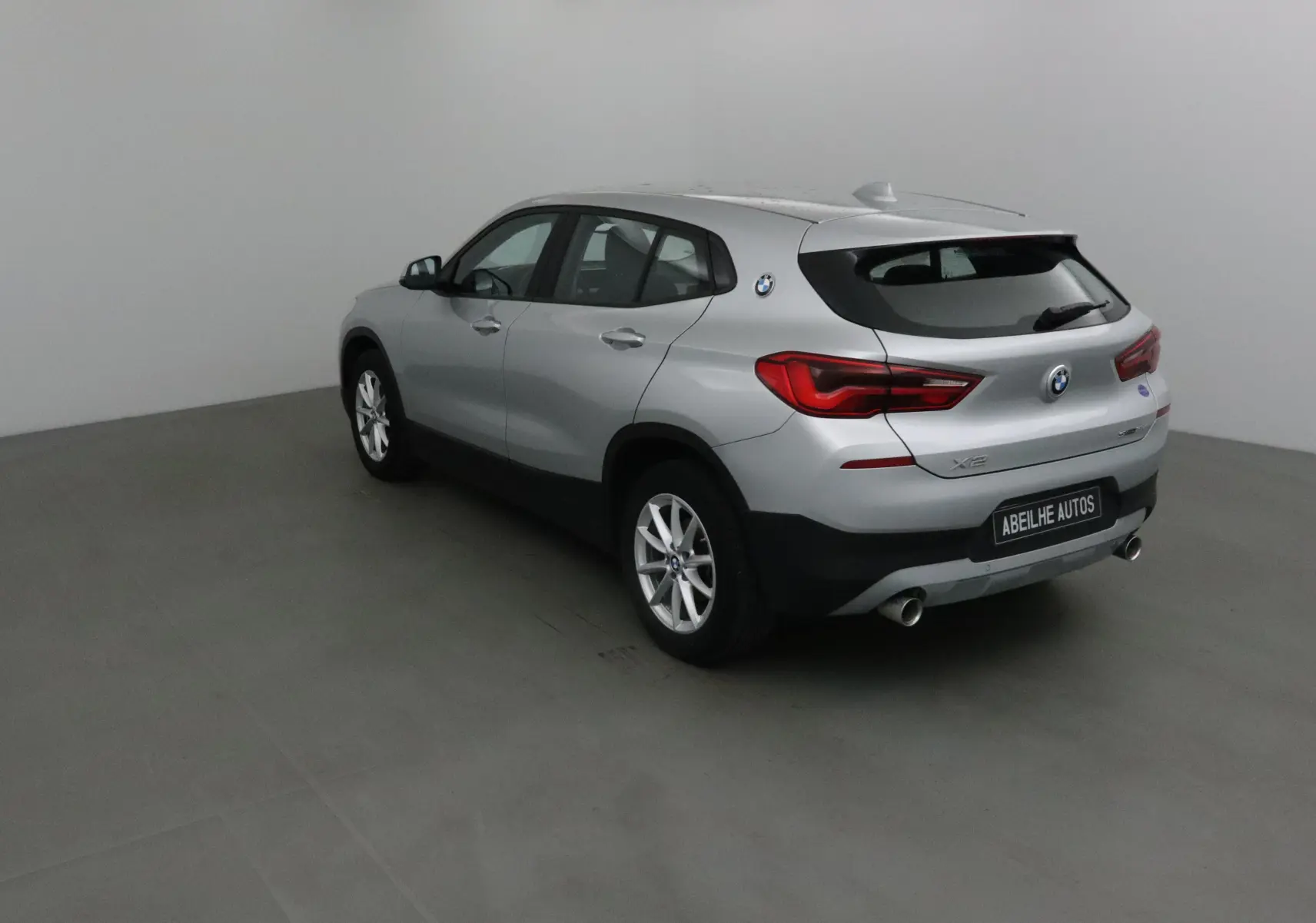 BMW X2 gris clair métal vue 3/4 arrière droit, avec feux arrière LED et double sortie d’échappement visible.