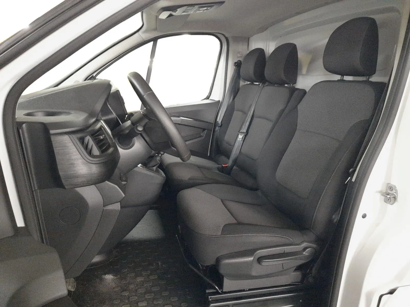 Vue intérieure côté conducteur du Renault Trafic Fourgon blanc 2024, montrant le tableau de bord et les sièges tissu noir et gris.