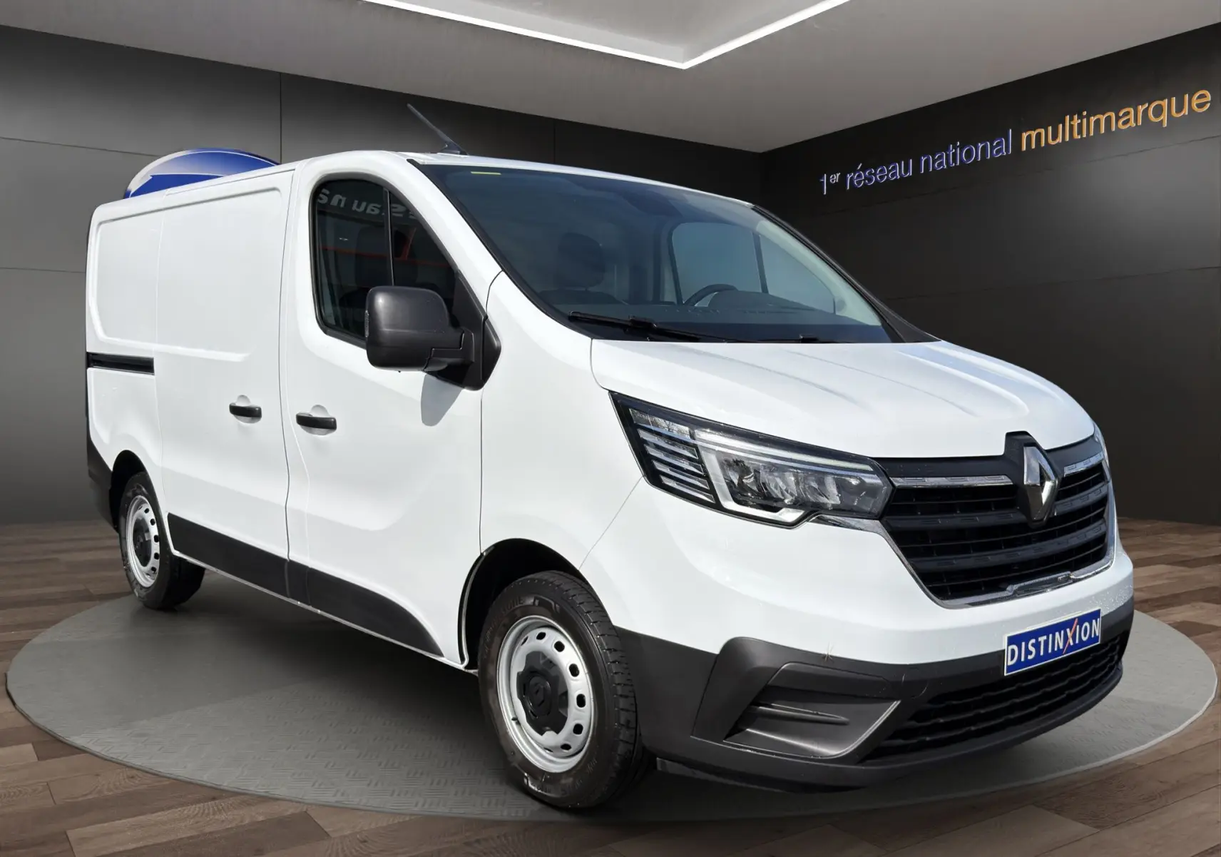 Renault Trafic Fourgon blanc en 3/4 avant droit, avec calandre noire et jantes acier visibles en intérieur showroom.