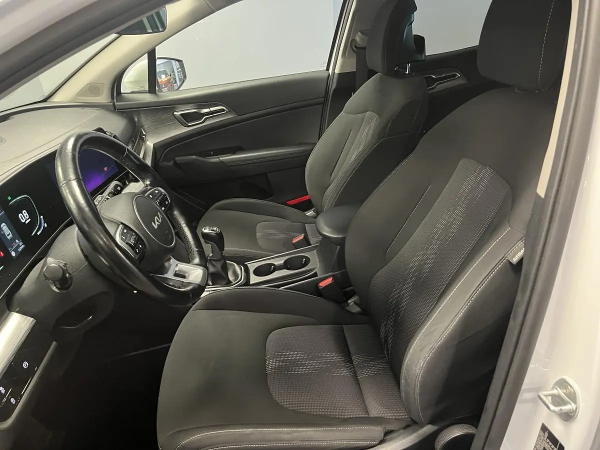 Intérieur avant du Kia Sportage blanc 2022, vue côté conducteur avec sièges noirs et volant cuir multifonction.