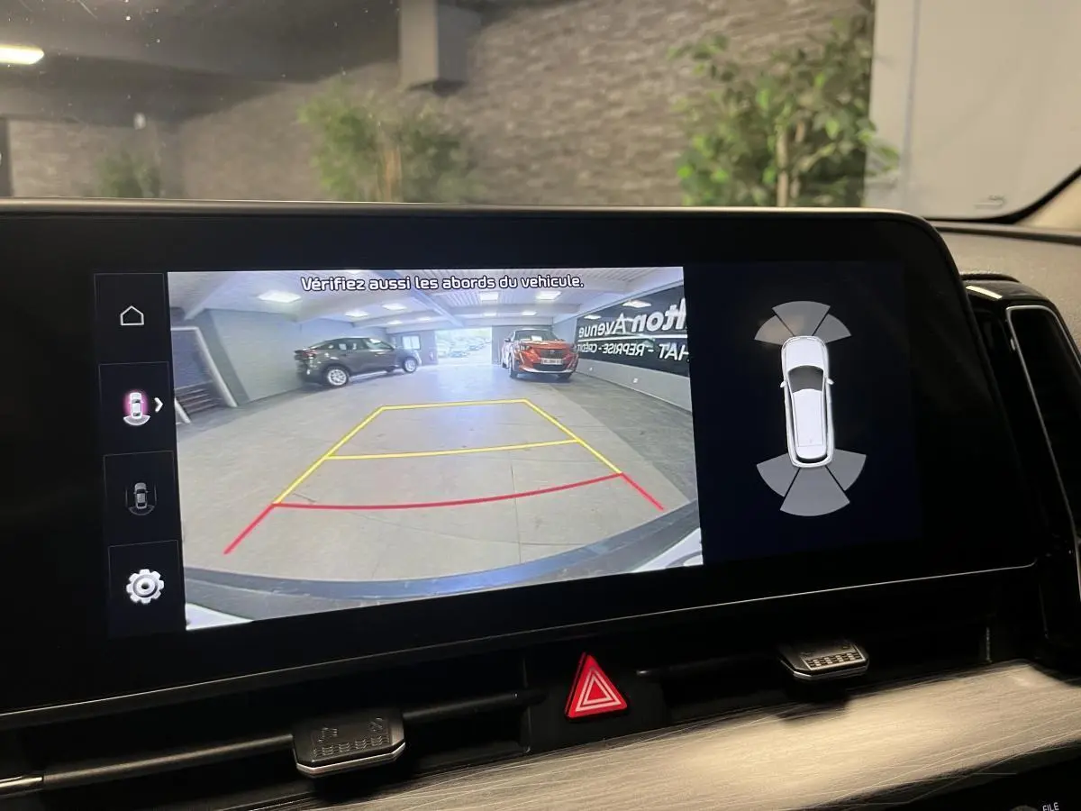 Écran tactile intérieur montrant la caméra de recul et l’aide au stationnement du Kia Sportage blanc, vue arrière.