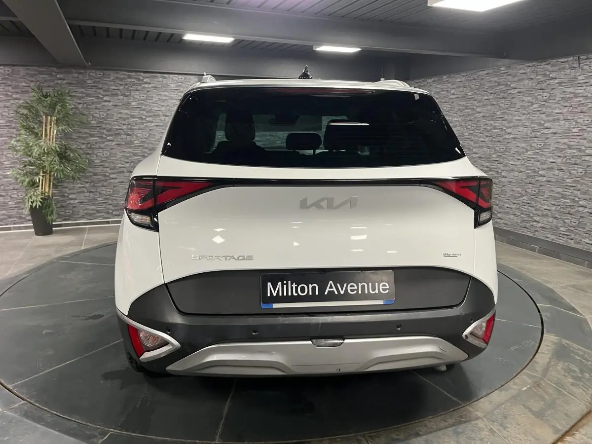 Vue arrière d'un KIA Sportage blanc nacré avec bouclier noir laqué et feux arrière LED en intérieur showroom.