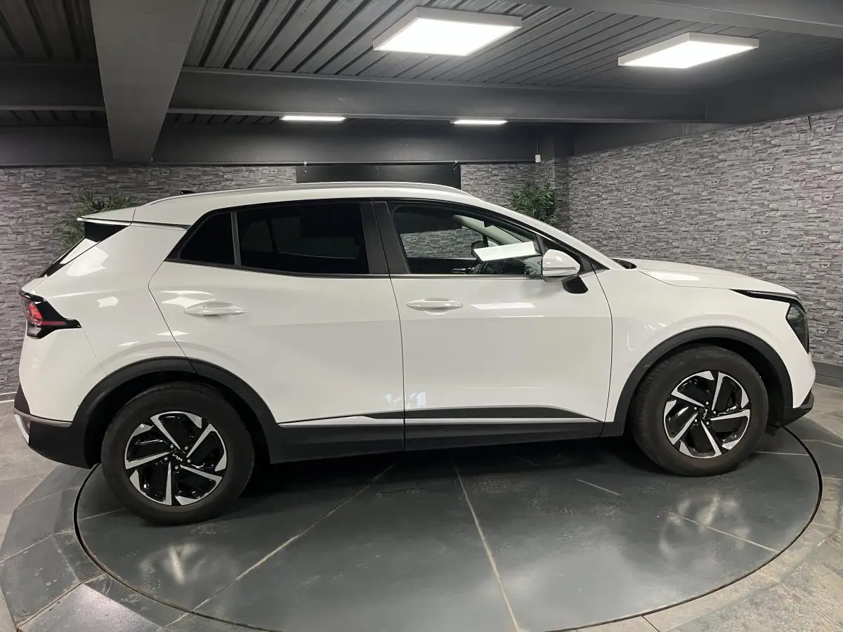 Vue latérale droite d’un KIA Sportage blanc nacré avec jantes alliage 18 pouces et vitres surteintées.