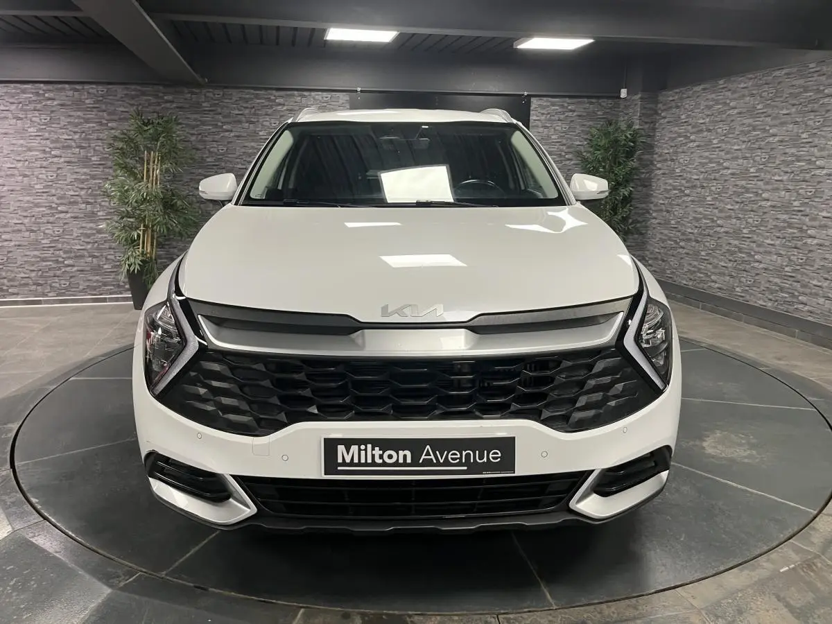 Vue avant d'un KIA SPORTAGE blanc nacré avec calandre noire laquée et feux LED en forme de boomerang.