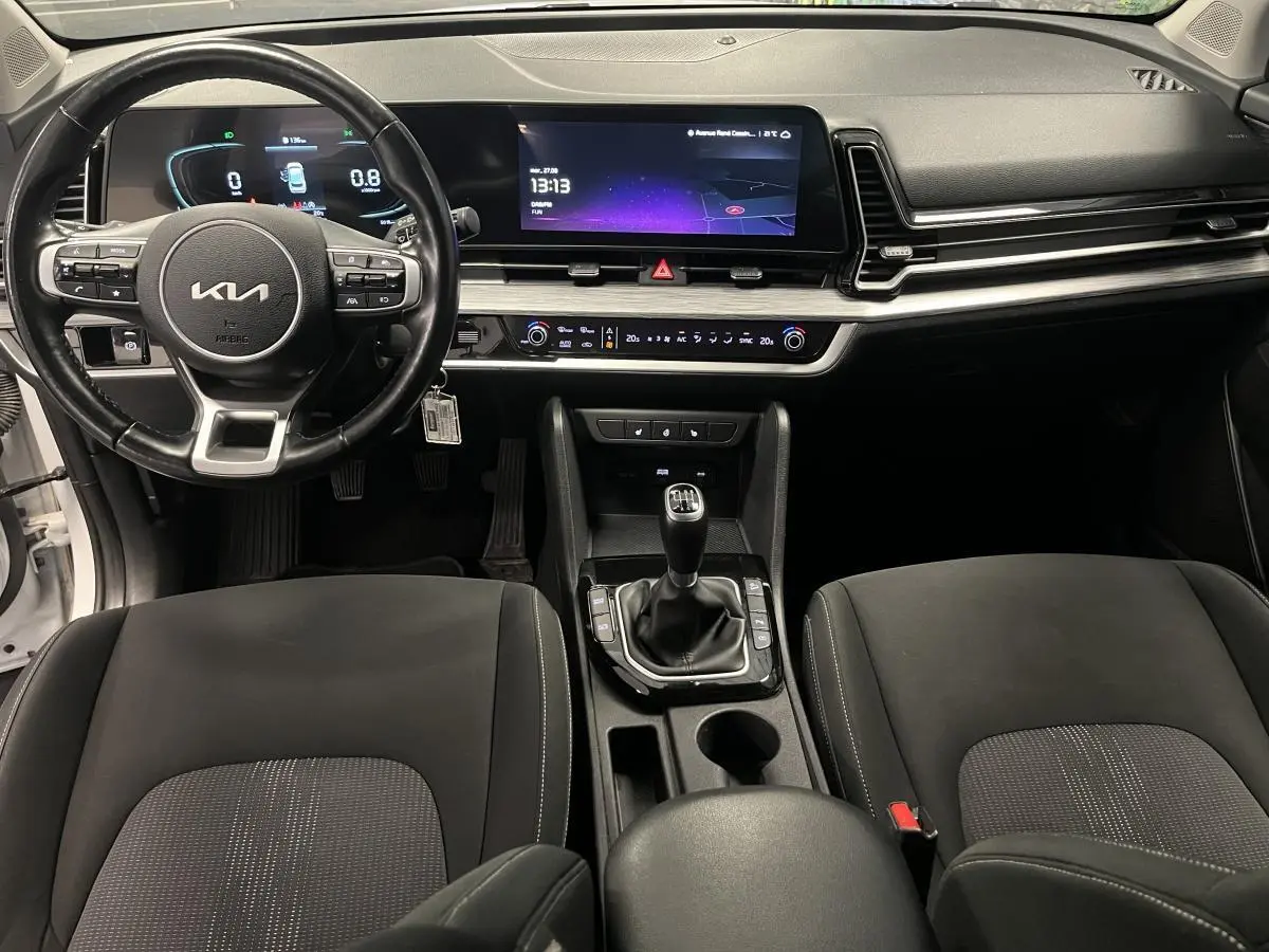 Vue intérieure avant du Kia Sportage 2022 blanc, avec tableau de bord digital et levier de vitesse manuel central.