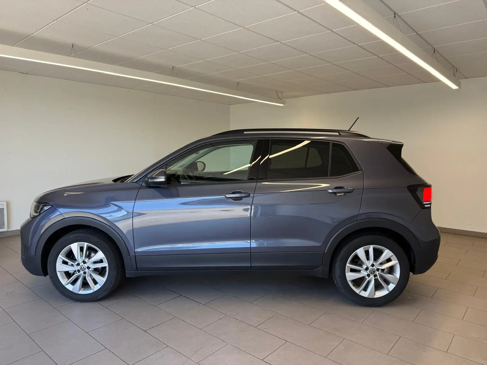 Profil côté gauche du Volkswagen T-Cross gris cendre 2025 en version 1.0 TSI 116 BVM6 VW EDITION, intérieur showroom.