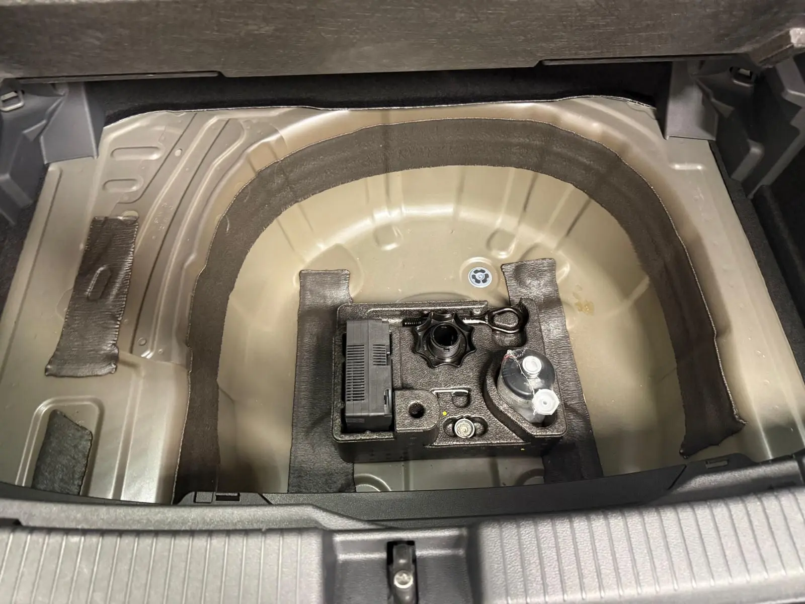 Coffre ouvert du Volkswagen T-Cross gris cendre 2025, vue plongeante sur le rangement sous plancher avec outils et compresseur.