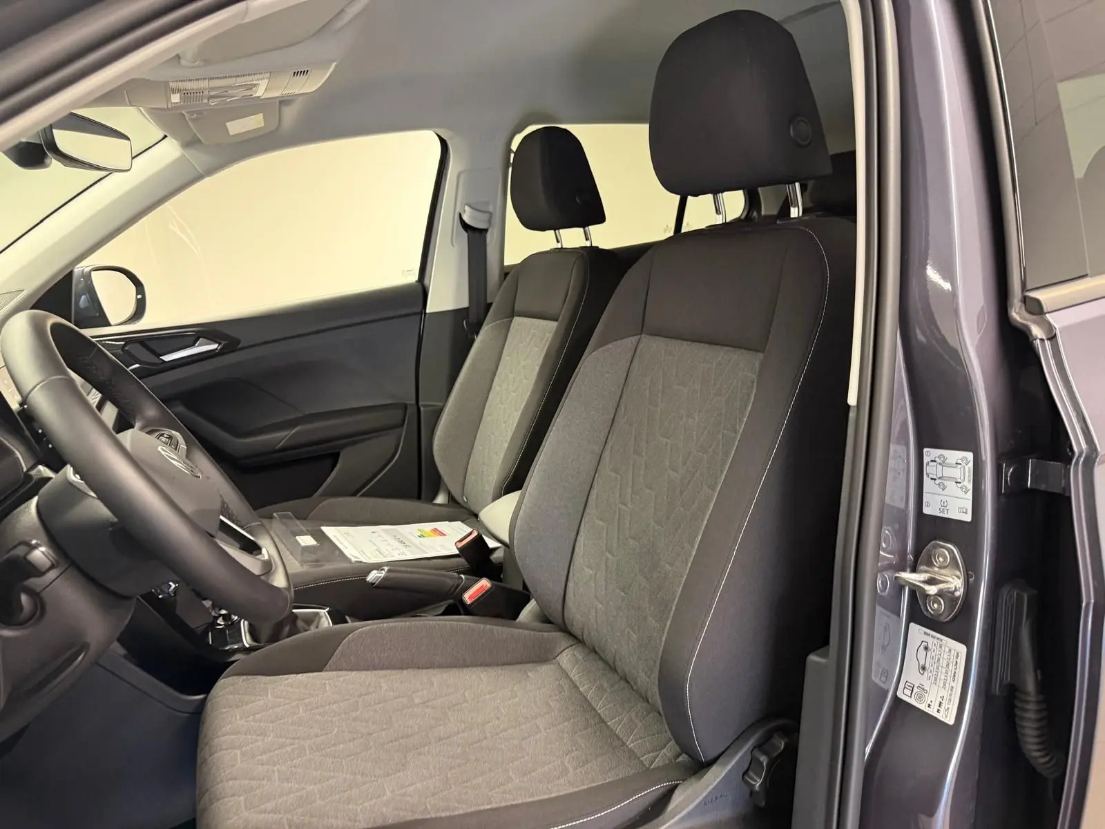 Intérieur du Volkswagen T-Cross gris cendre 2025, vue côté conducteur ouverte, sièges tissu gris avec motifs géométriques.