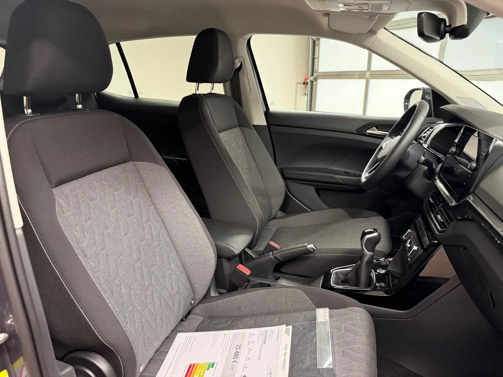 Vue intérieure côté conducteur du Volkswagen T-Cross gris cendre 2025, montrant les sièges tissu et la boîte manuelle.