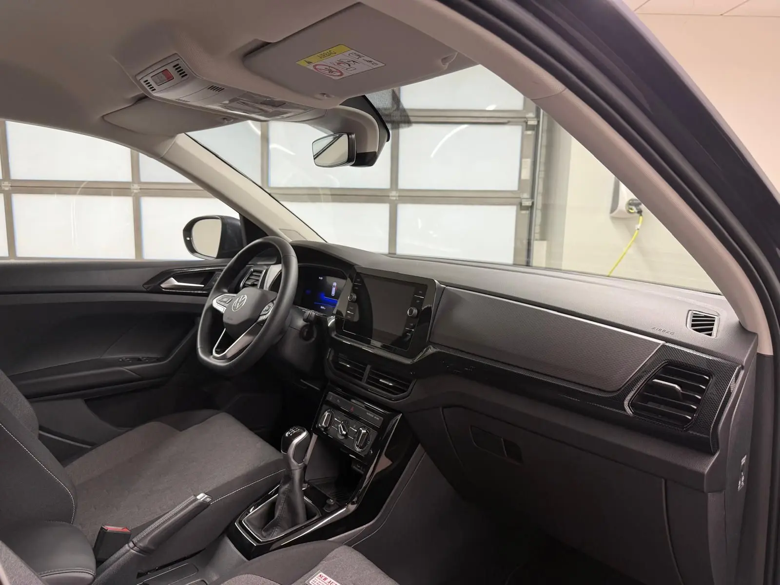 Vue intérieure côté conducteur du Volkswagen T-Cross 2025, avec tableau de bord noir et sièges gris foncé.