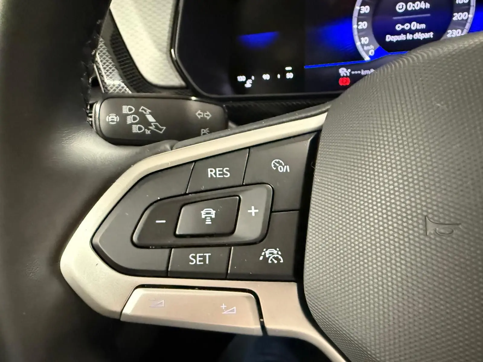 Gros plan sur les commandes au volant du Volkswagen T-Cross 2025, avec boutons de régulateur et affichage numérique bleu.