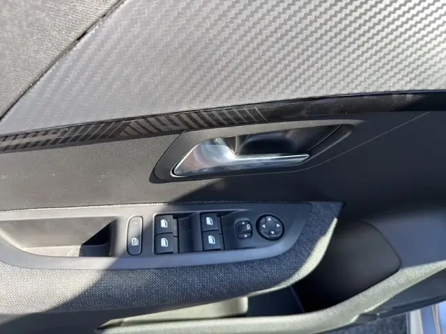 Gros plan sur la porte côté conducteur d'une Peugeot 208 gris clair, avec commandes électriques et poignée chromée.