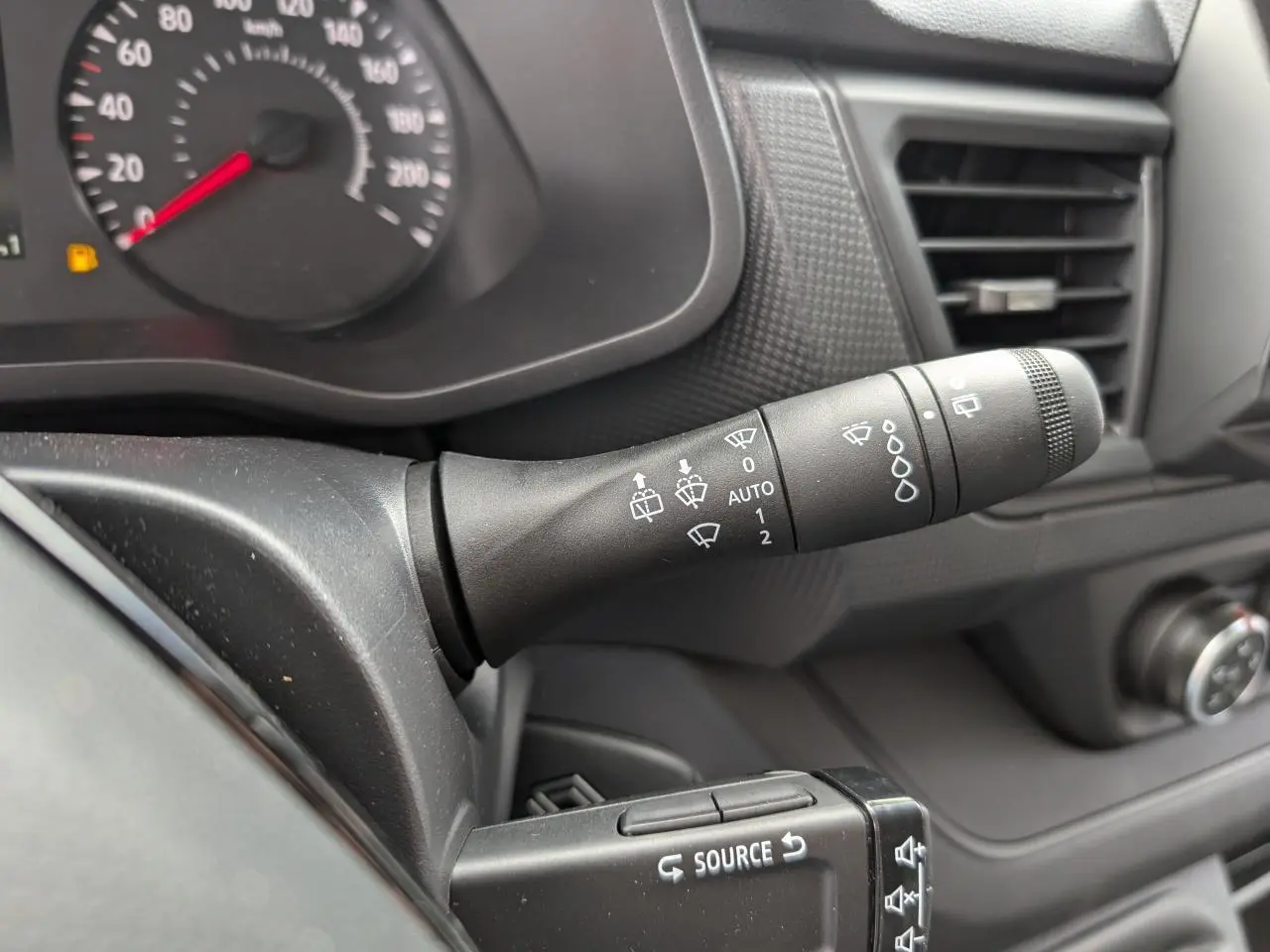 Gros plan sur la manette d’essuie-glace noire du tableau de bord du Renault Trafic Fourgon gris, avec compteur partiel.