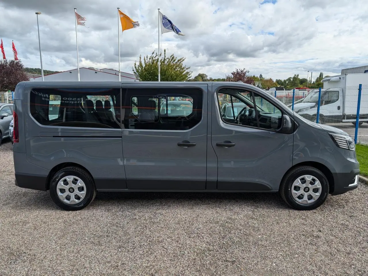 Profil droit d’un Renault Trafic Fourgon L2 gris avec vitres latérales et jantes argentées, stationné en extérieur.