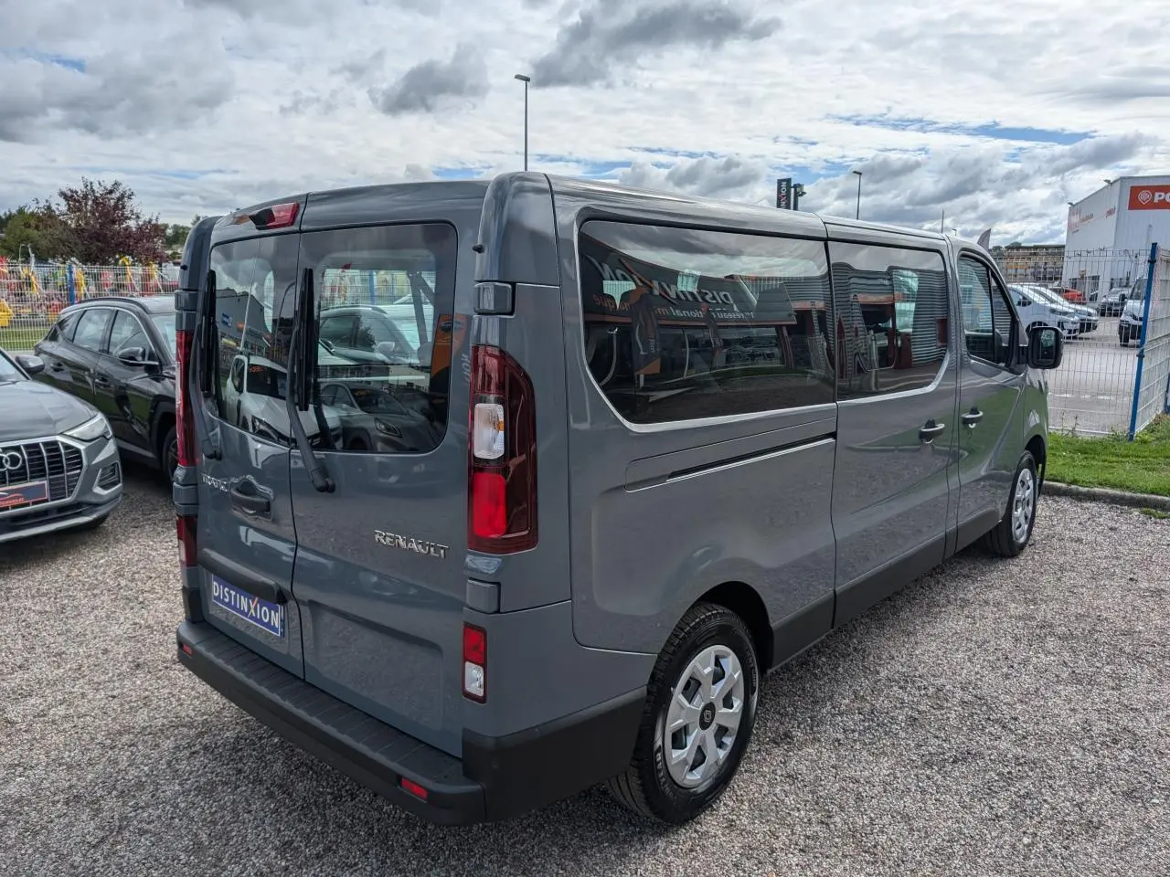 Vue 3/4 arrière droite du Renault Trafic Fourgon gris avec vitres latérales et hayon vitré, stationné sur gravier.