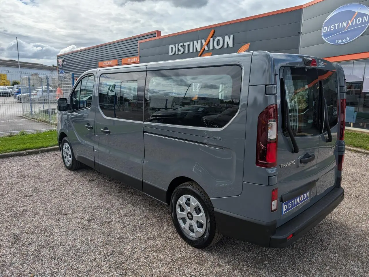 Vue 3/4 arrière droite du Renault Trafic Fourgon gris avec vitres latérales et jantes avec enjoliveurs sur parking.