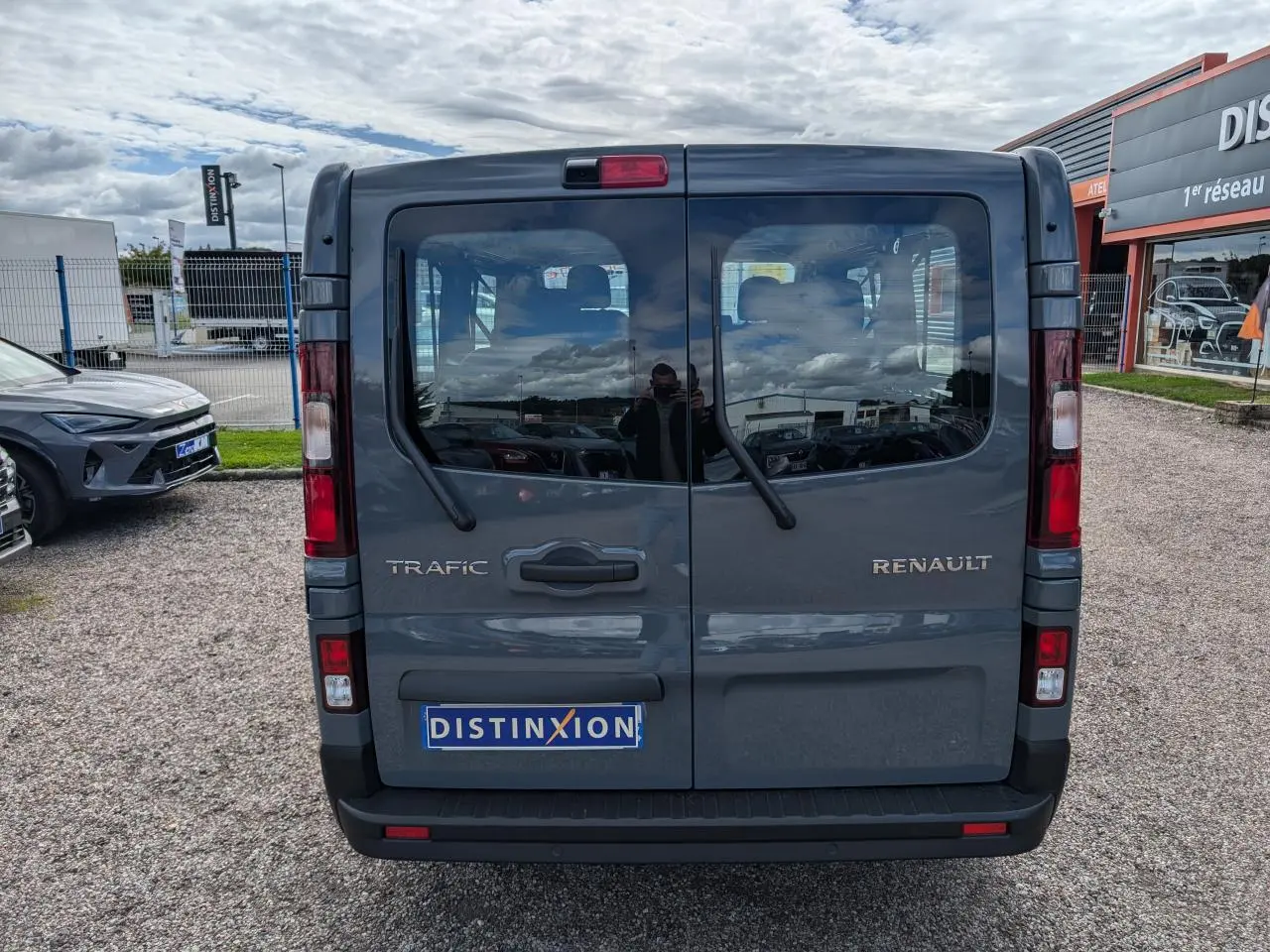 Vue arrière d'un Renault Trafic Fourgon gris avec portes battantes et logo distinctif sur parking.