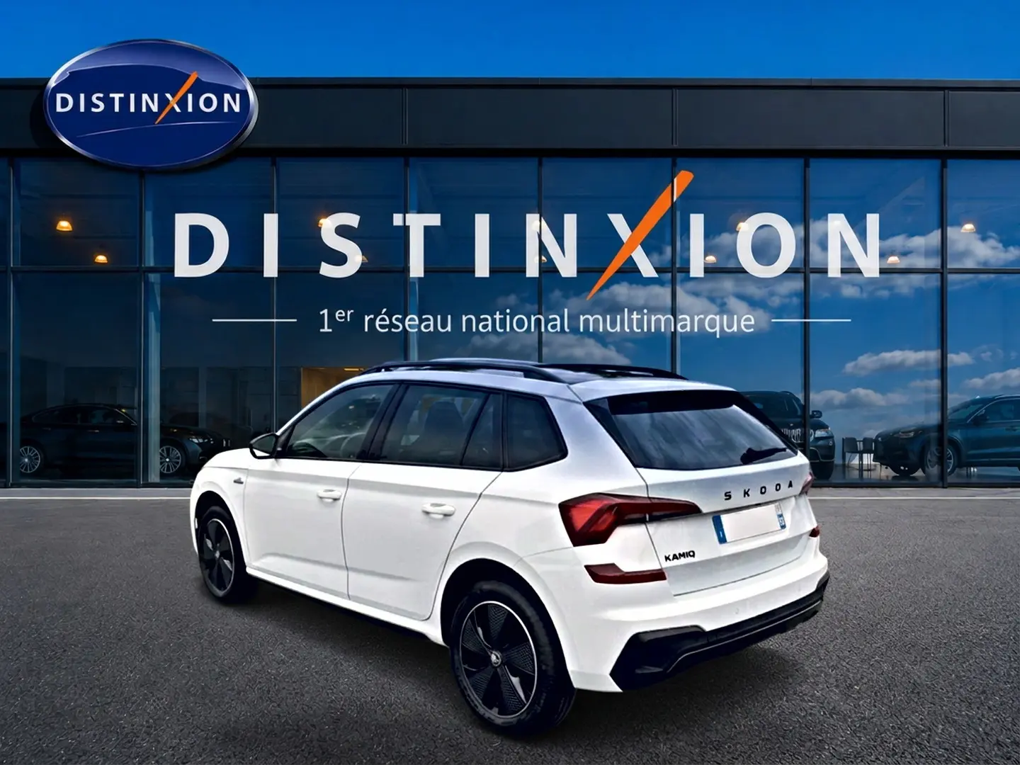 Vue 3/4 arrière droite du Skoda Kamiq blanc nacré avec jantes noires et toit panoramique, devant une vitrine Distinxion.