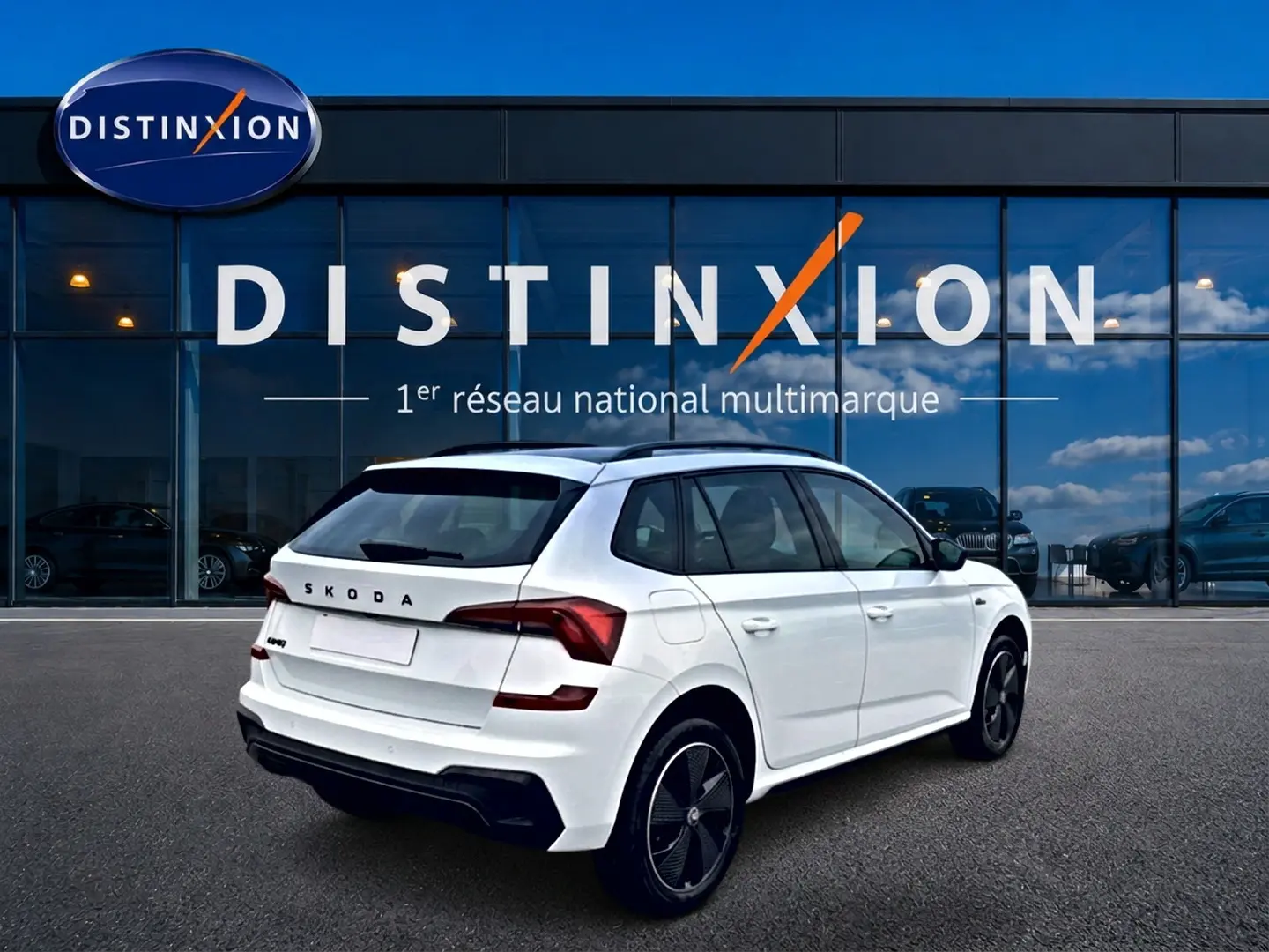 Vue 3/4 arrière droite d'un Skoda Kamiq blanc nacré avec jantes noires, devant une vitrine Distinxion.