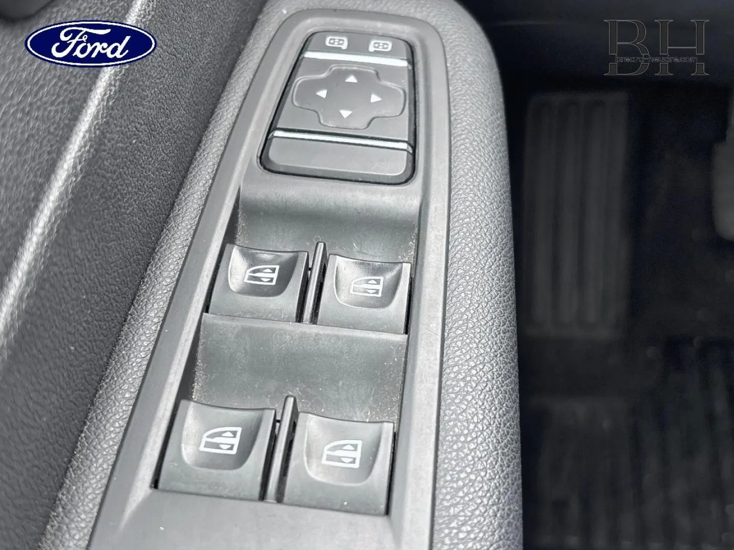 Panneau de commandes des vitres électriques côté conducteur d’un véhicule, avec boutons noirs sur plastique gris texturé.