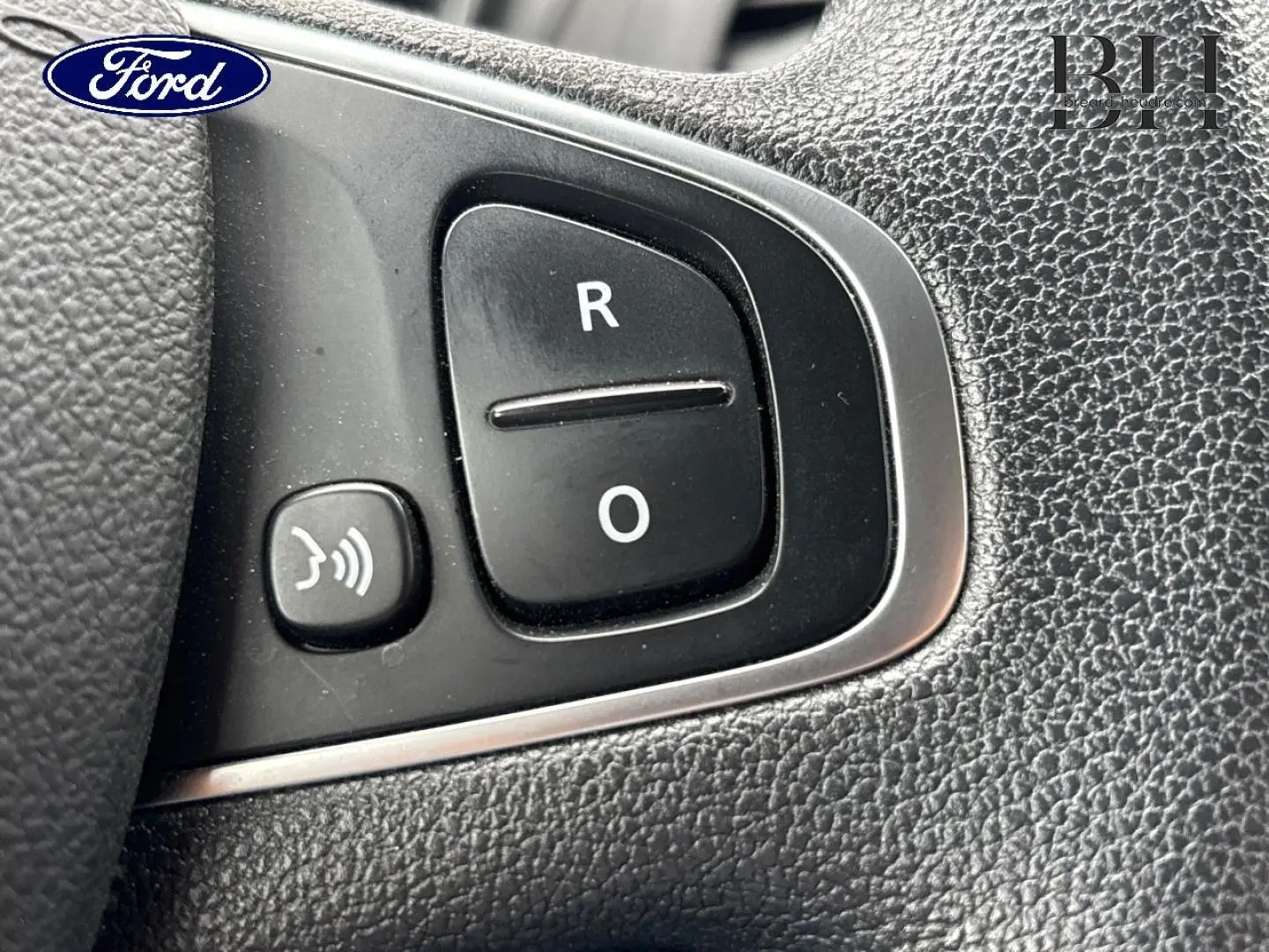 Gros plan sur les boutons de commande vocale et radio au volant d'un véhicule, finition noire texturée.