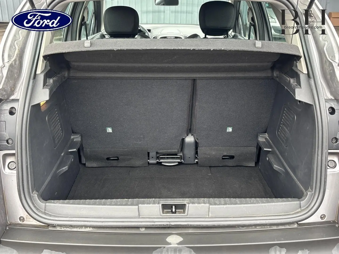 Coffre ouvert d’un Renault Captur gris Cassiopée, vue arrière montrant la banquette arrière et le plancher de coffre vide.
