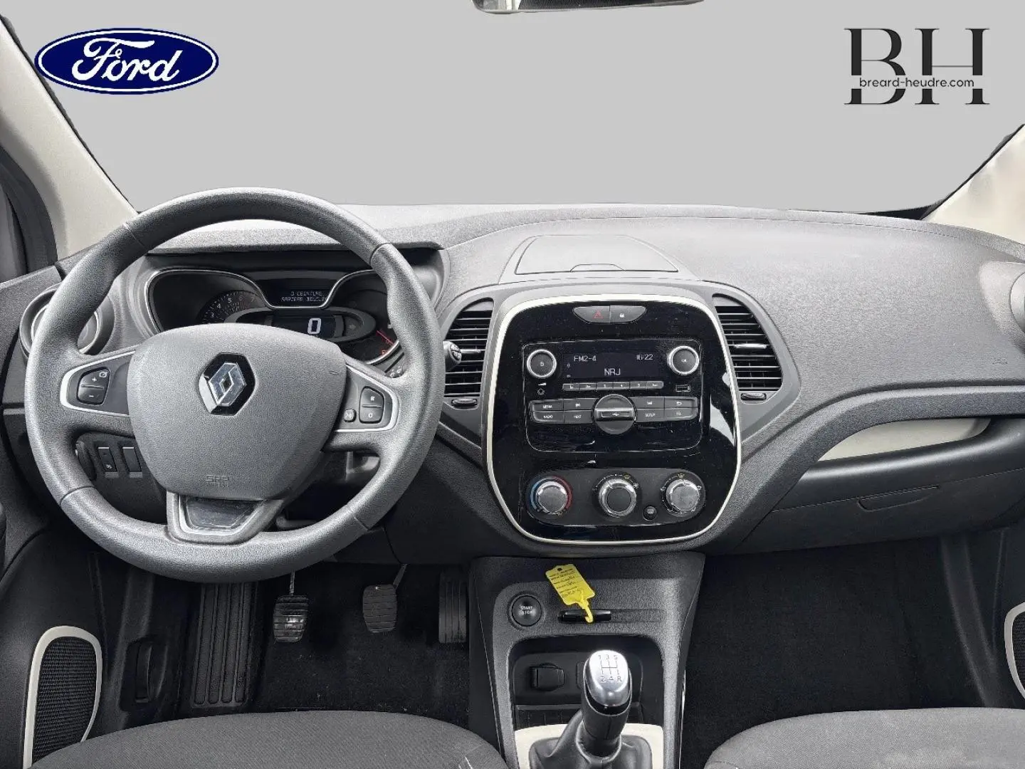 Vue intérieure avant du tableau de bord gris et volant Renault avec levier de vitesse manuel et écran central tactile.