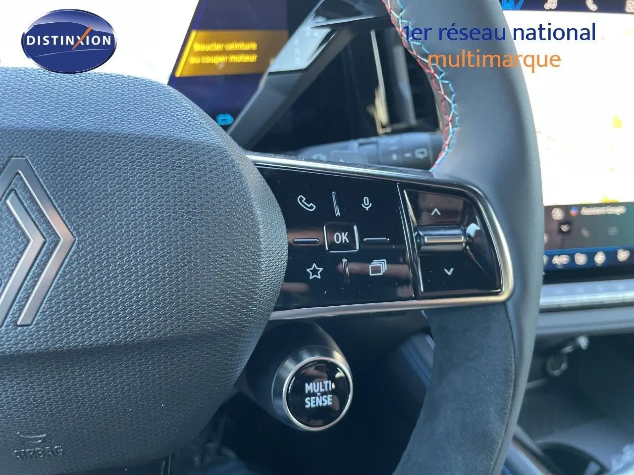 Gros plan sur le volant noir avec surpiqûres tricolores du Renault Austral E-Tech, mettant en valeur les commandes multifonctions et le bouton Multi-Sense.