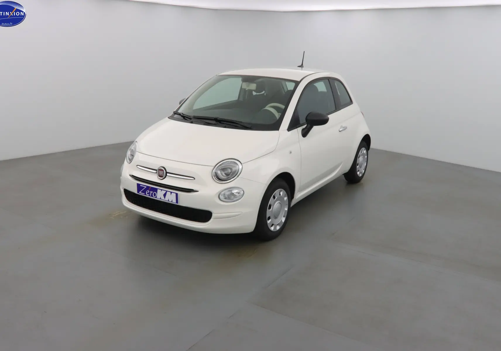 Fiat 500 blanc gelato vue 3/4 avant droit dans un studio lumineux avec jantes acier et rétroviseurs noirs.