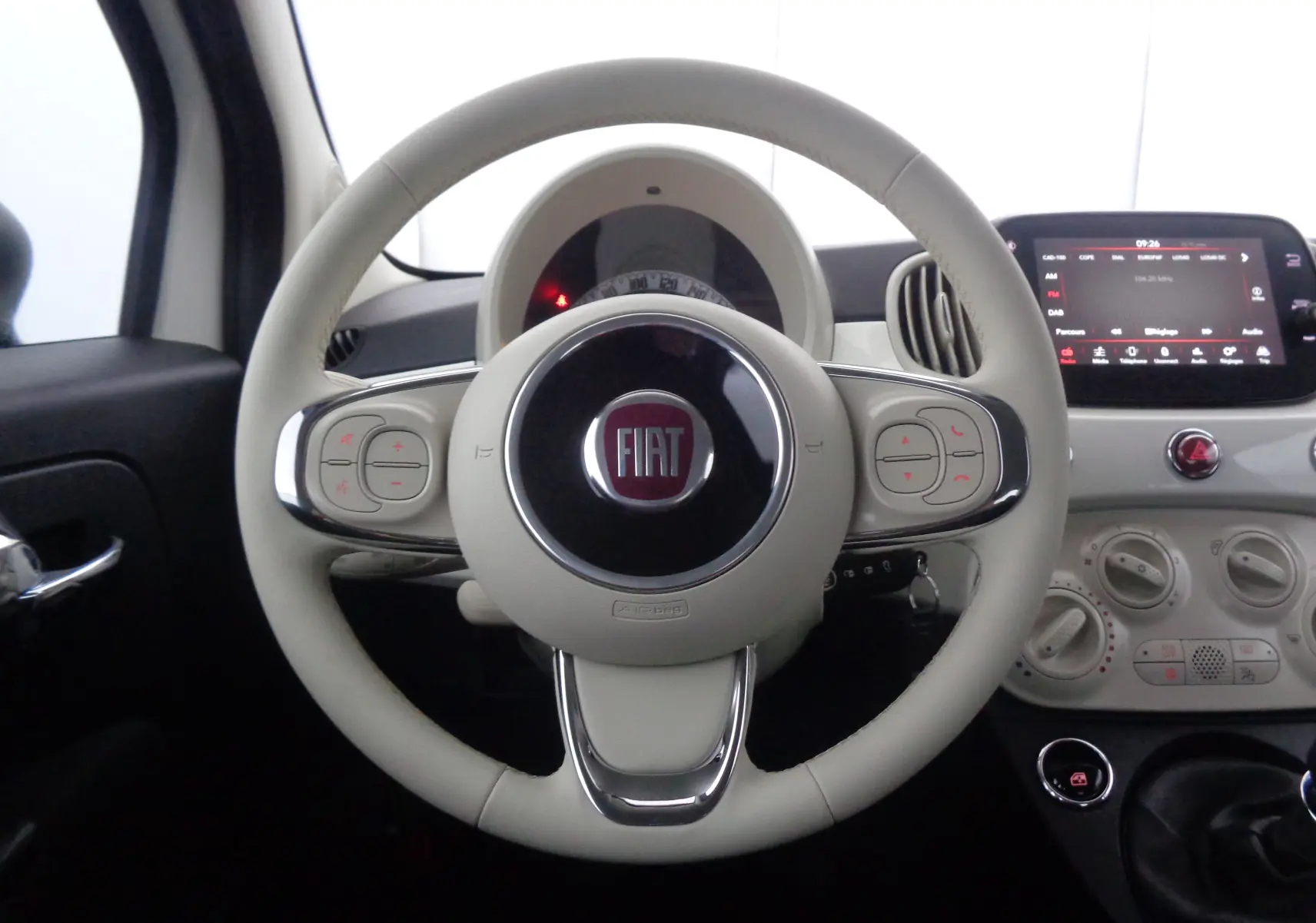 Vue rapprochée du volant blanc crème de la FIAT 500 1.0 Hybrid 2023 avec tableau de bord et écran tactile.