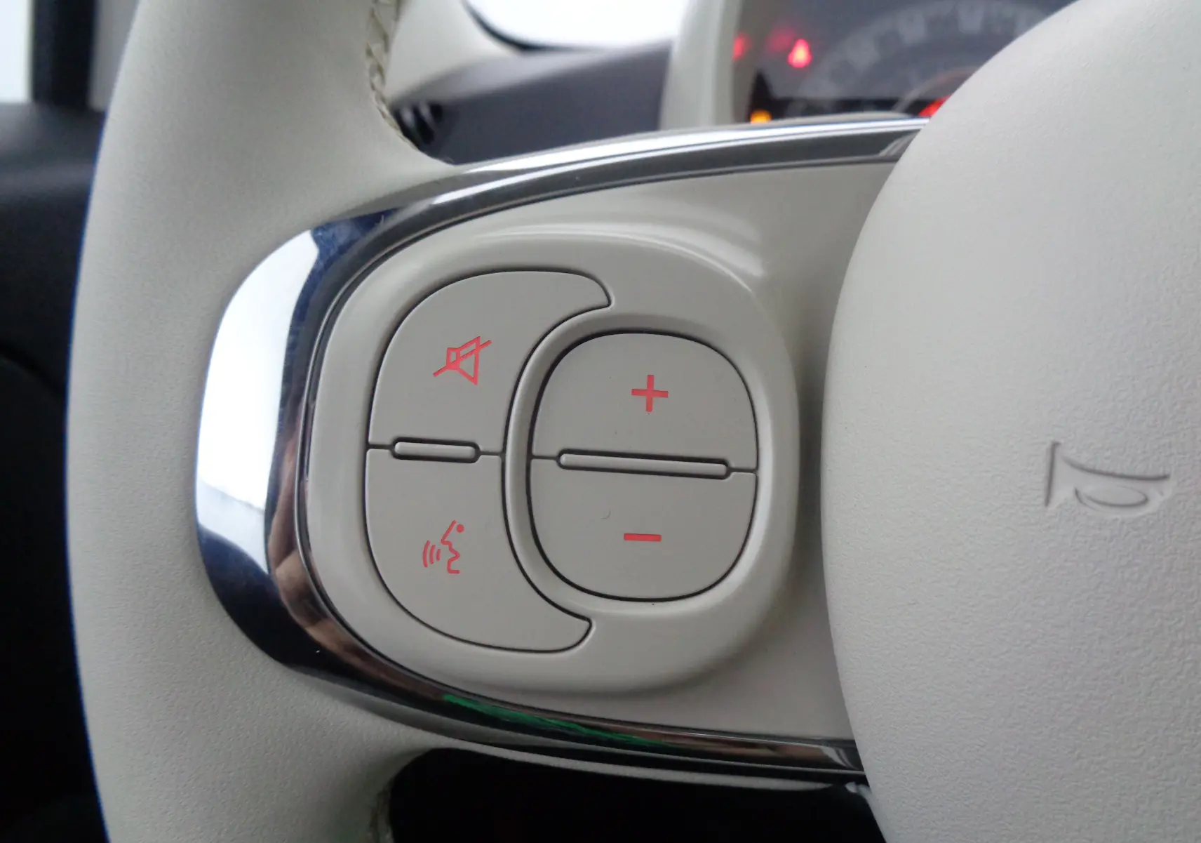 Gros plan sur les commandes de volume et de coupure du son sur le volant blanc de la Fiat 500 1.0 Hybrid 2023.