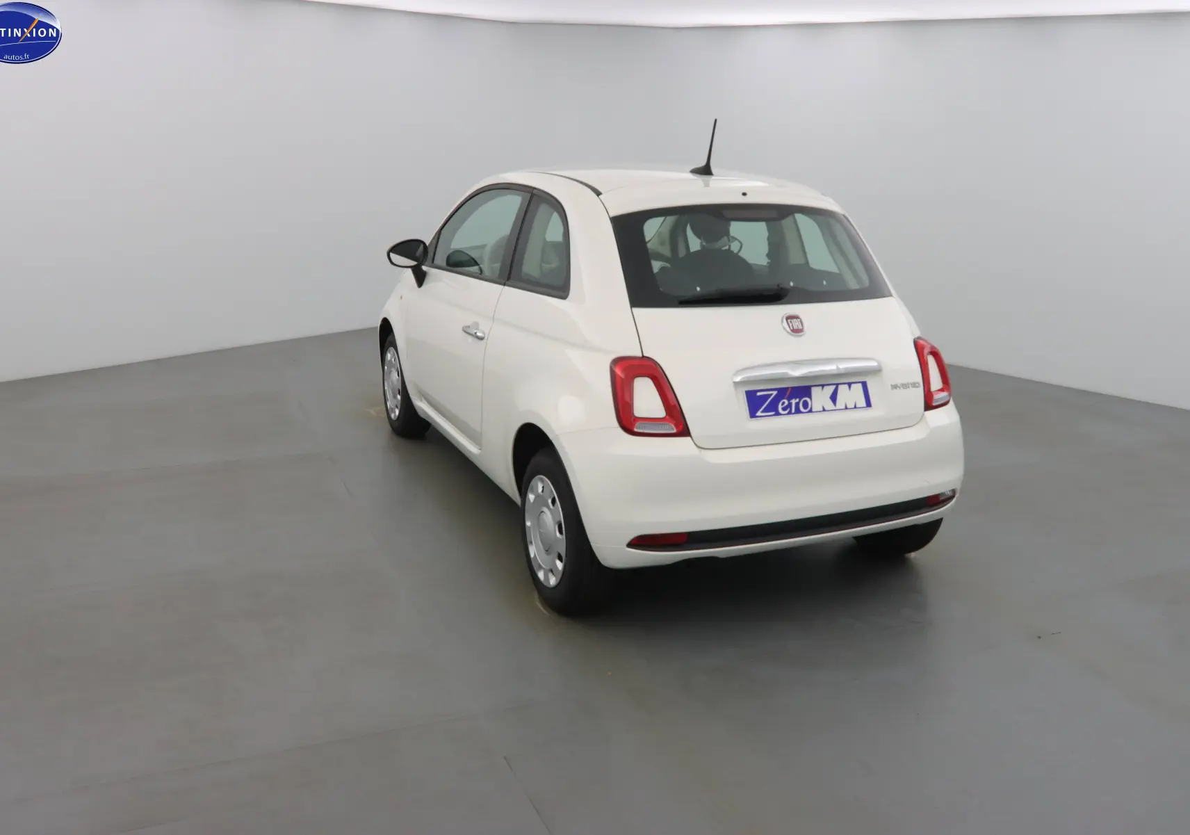 Fiat 500 blanc gelato vue 3/4 arrière gauche dans un studio, avec plaque "Zero KM" visible.