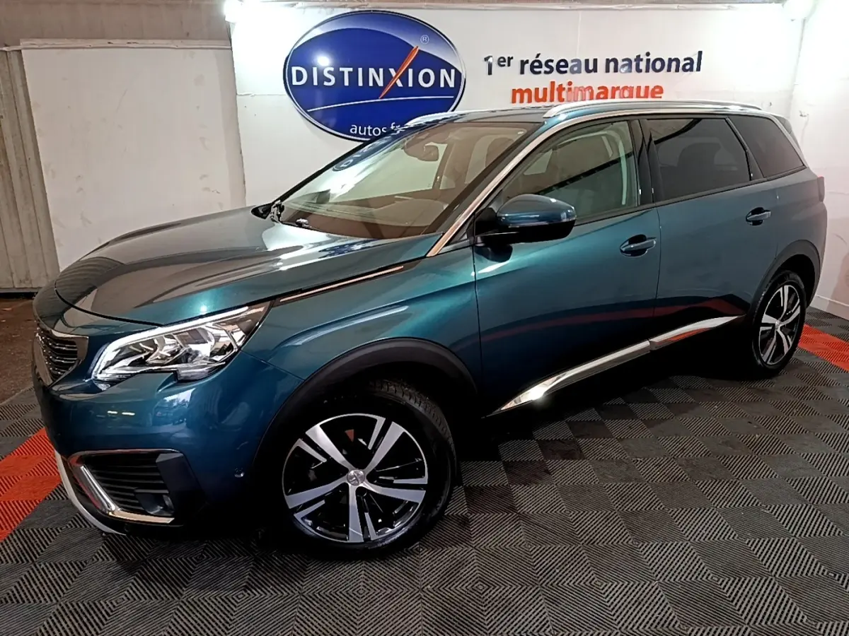 Peugeot 5008 bleu en 3/4 avant droit, avec jantes alliage et calandre distinctive dans un showroom.
