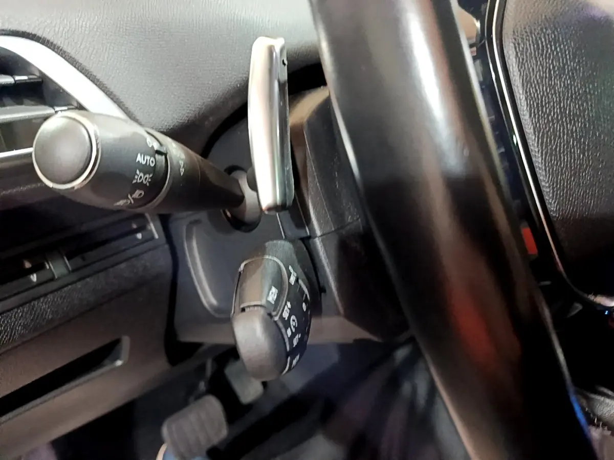 Gros plan sur la colonne de direction et commandes derrière le volant cuir noir du Peugeot 5008 bleu, version 2018.