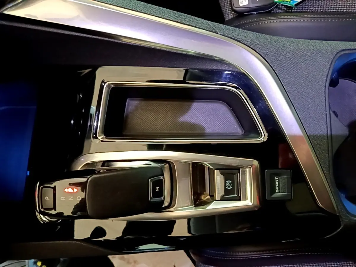 Gros plan sur la console centrale noire brillante du Peugeot 5008 bleu, montrant le levier de boîte automatique et bouton sport.