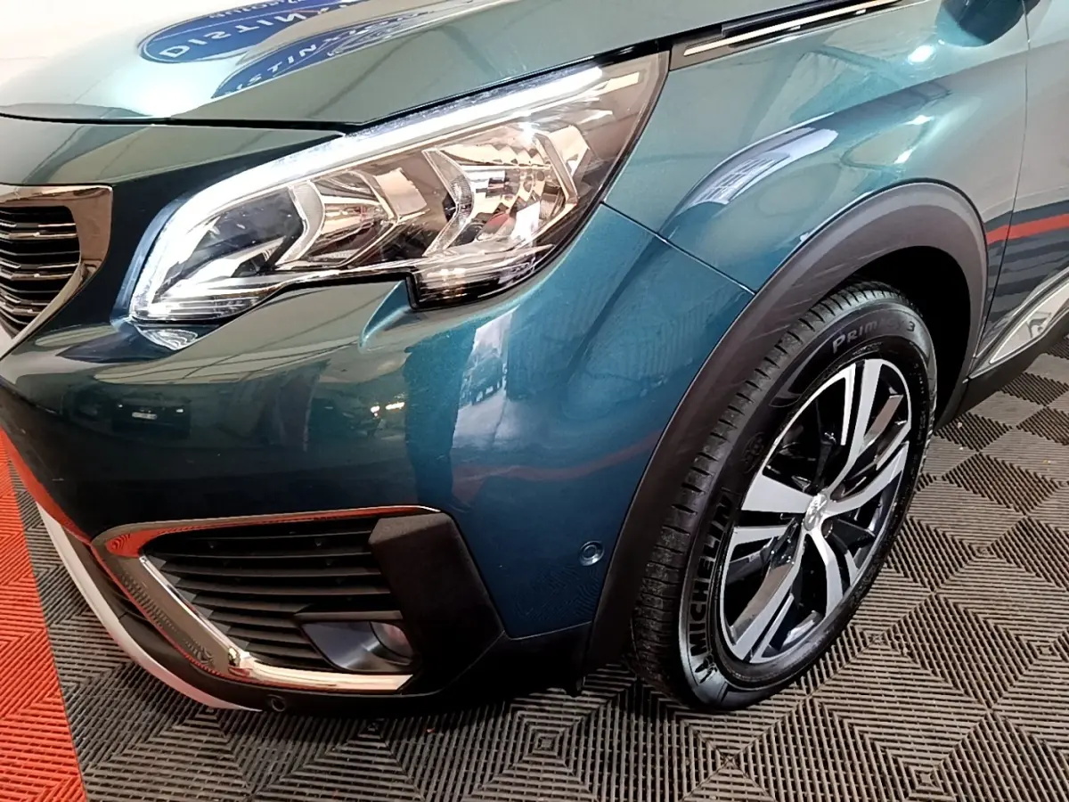 Gros plan sur l'avant droit bleu métallisé du Peugeot 5008 avec phare et jante alliage visible.